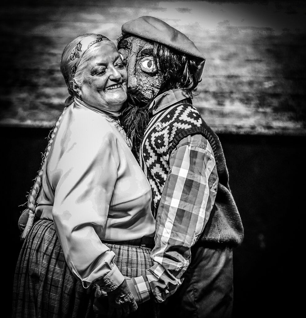 Older woman embracing masked folkloric performer during public cultural event