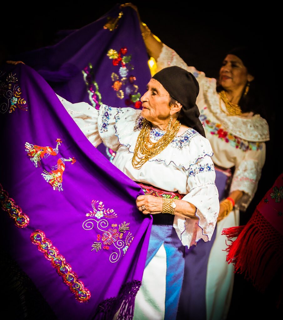 Elder woman holding embroidered ceremonial textile during public event